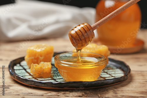 Honey dripping from wooden dipper into glass bowl on table, closeup