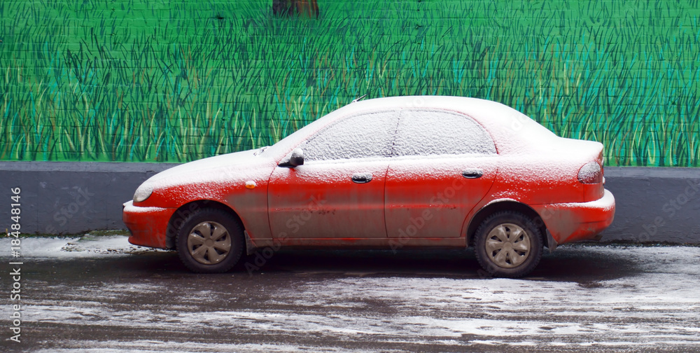 A lonely dirty red car, powdered with snow