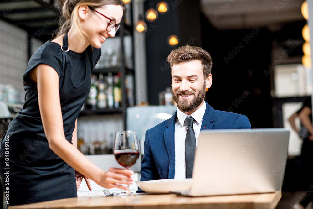 Young woman waitress bringing a glass of red wine for a businessman at the restaurant Young woman waitress bringing a glass of red wine for a businessman at the restaurant