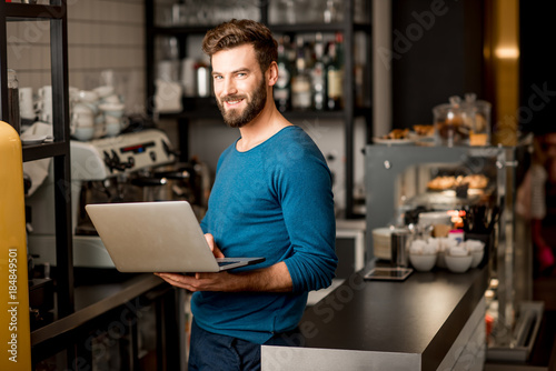 Handsome man in blue sweater working with laptop at the bar of the modern cafe interior