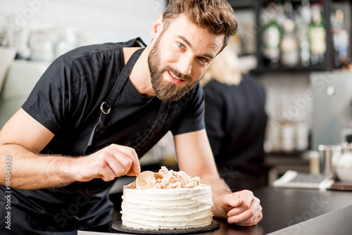 Handsome confectioner in black t-shirt decorating a pie at the bar of the modern cafe interior photo
