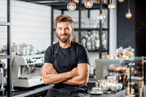 Portrait of a handsome barista in black t-shirt and apron sitting at the bar of the modern cafe photo