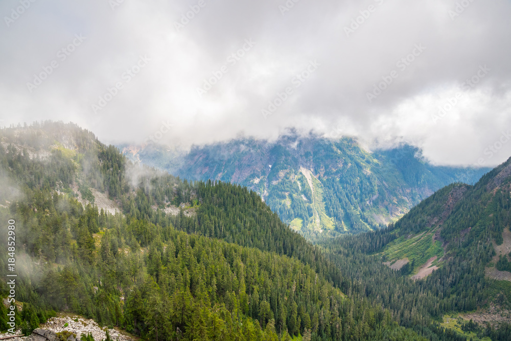 Beautiful rocky mountains with blue sky on the background and white clouds covering green forest