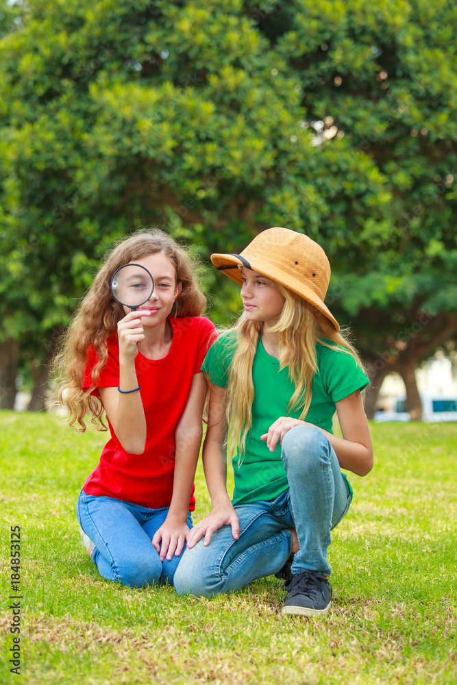 Two school girls exploring the nature with magnifying glass