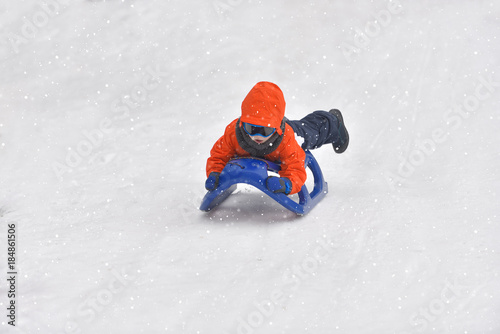 Little boy riding on snow slides in winter time