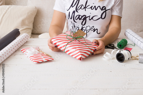 Woman holding Christmas gift wrapped in striped paper and decorated with twine and tag. Girl wrapping presents for the party.