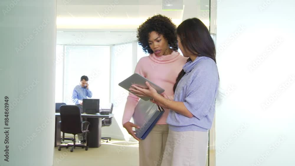 Two businesswomen talking in office with man in background