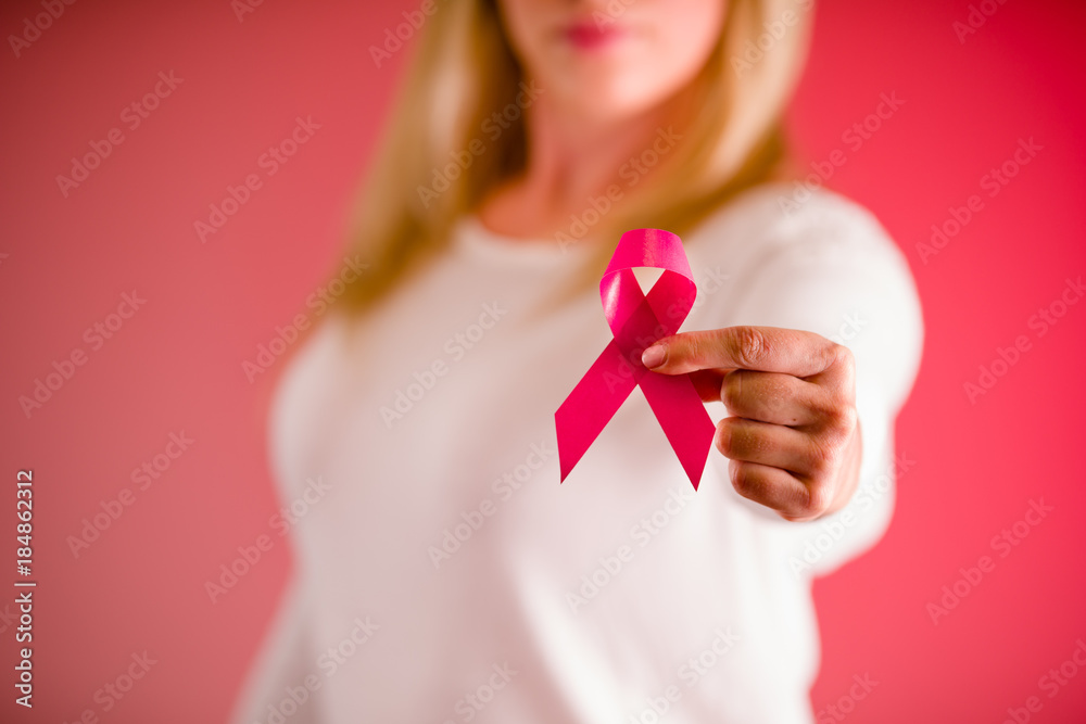Close up of a beautiful woman wearing a white blouse and holding a pink breast cancer awareness ribbon in her hand, cancer concept in a pink background Close up of a beautiful woman wearing a white blouse and holding a pink breast cancer awareness ribbon in her hand, cancer concept in a pink background