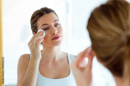 Beautiful young woman is cleaning her face while looking in the mirror in the bathroom.