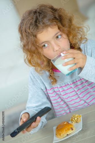 Young girl having snack, holding remote control