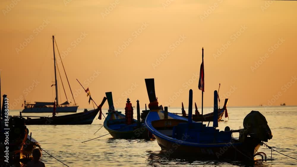 Group of silhouette long tail boat converted to boat excursions floating in the andaman sea with golden light of the Sun before sunset and yatch boat background in travel or transportation concept. Group of silhouette long tail boat converted to boat excursions floating in the andaman sea with golden light of the Sun before sunset and yatch boat background in travel or transportation concept.