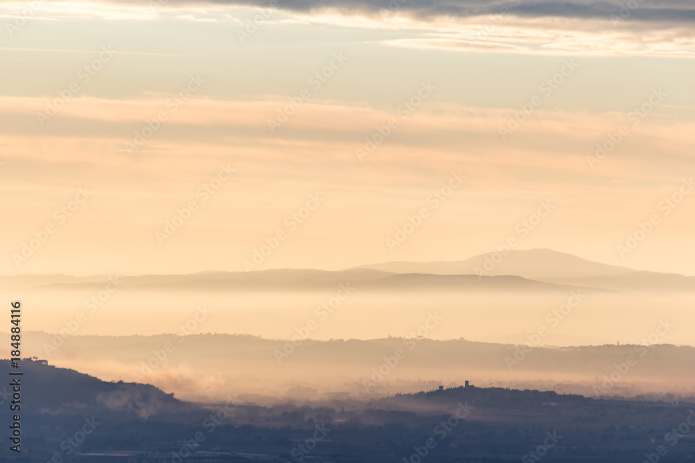 Umbria valley in autumn filled by mist at sunset, with emerging hills and towns and beautiful warm, orange tones