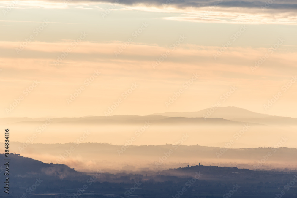Umbria valley in autumn filled by mist at sunset, with emerging hills and towns and beautiful warm, orange tones Umbria valley in autumn filled by mist at sunset, with emerging hills and towns and beautiful warm, orange tones