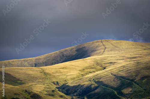 Golden light shining on hill near Sedbergh with dark clouds in background