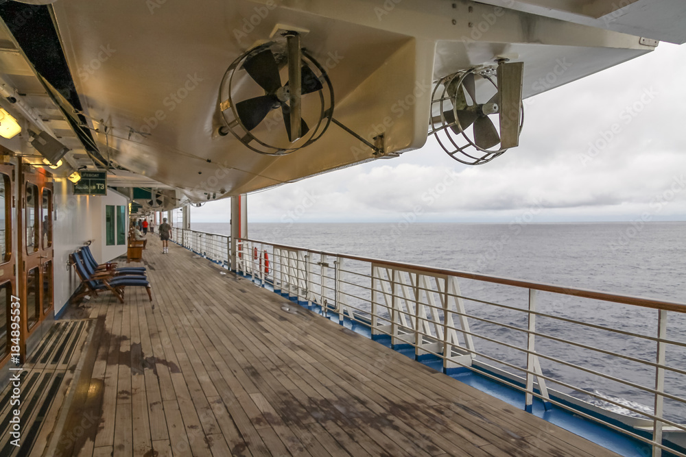 Teak lined Promenade Deck of modern cruise ship on a grey stormy day.