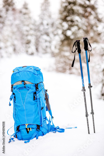 Blue backpack and tracking sticks at the snowy fir forest. Winter hiking concept