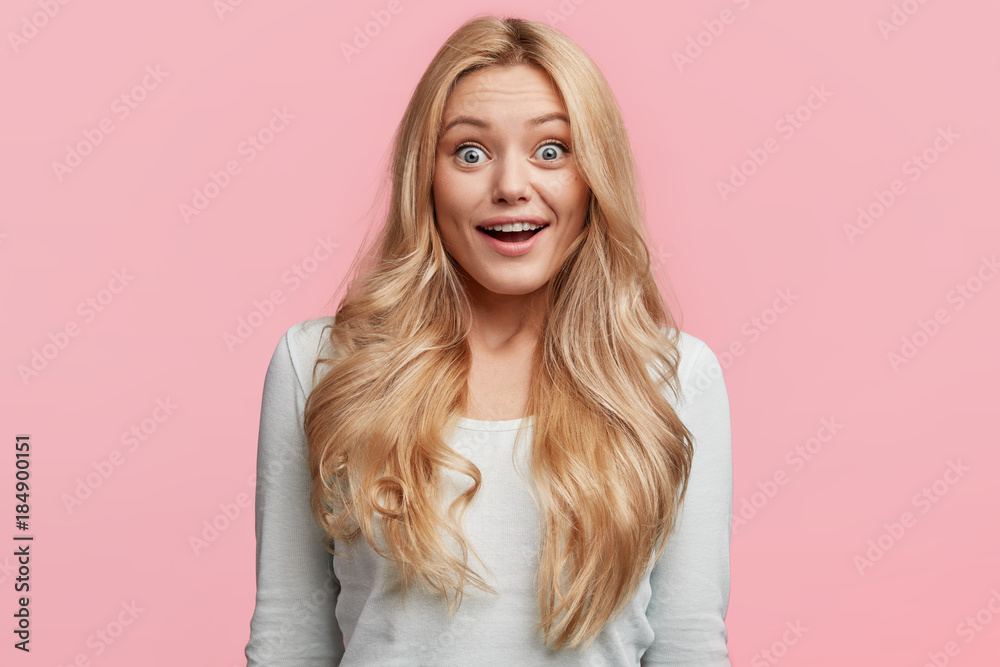 Φωτογραφία Indoor shot of stupefied blonde beautiful young woman with long hair looks with great surprisment at camera, recieves news from best friend, gossips about boys, isolated over pink backgroud