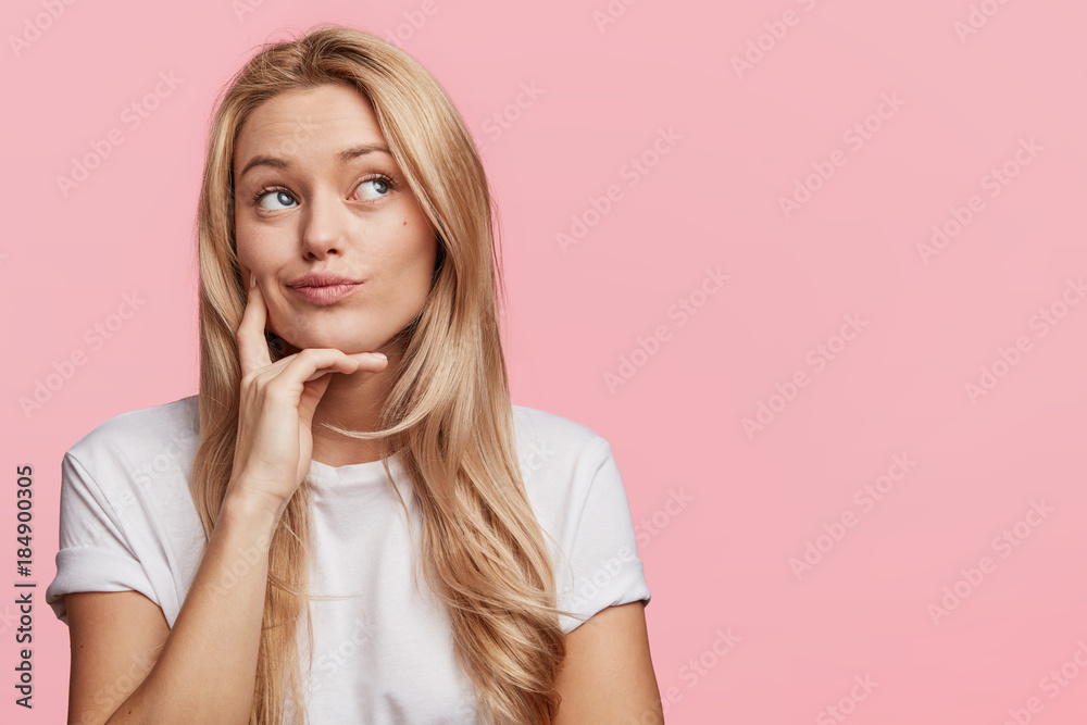 Horizontal shot of beautiful thoughtful woman looks pensively aside, being deep in thoughts, analyzes something in her mind, isolated over pink background with copy space for your promotional text Horizontal shot of beautiful thoughtful woman looks pensively aside, being deep in thoughts, analyzes something in her mind, isolated over pink background with copy space for your promotional text