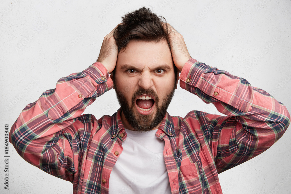 Headshot of young bearded male with annoyed expression, scratches head and screams loudly, regrets wrong doing or mistakes, isolated over white background. Negative human emotions, reaction concept Headshot of young bearded male with annoyed expression, scratches head and screams loudly, regrets wrong doing or mistakes, isolated over white background. Negative human emotions, reaction concept