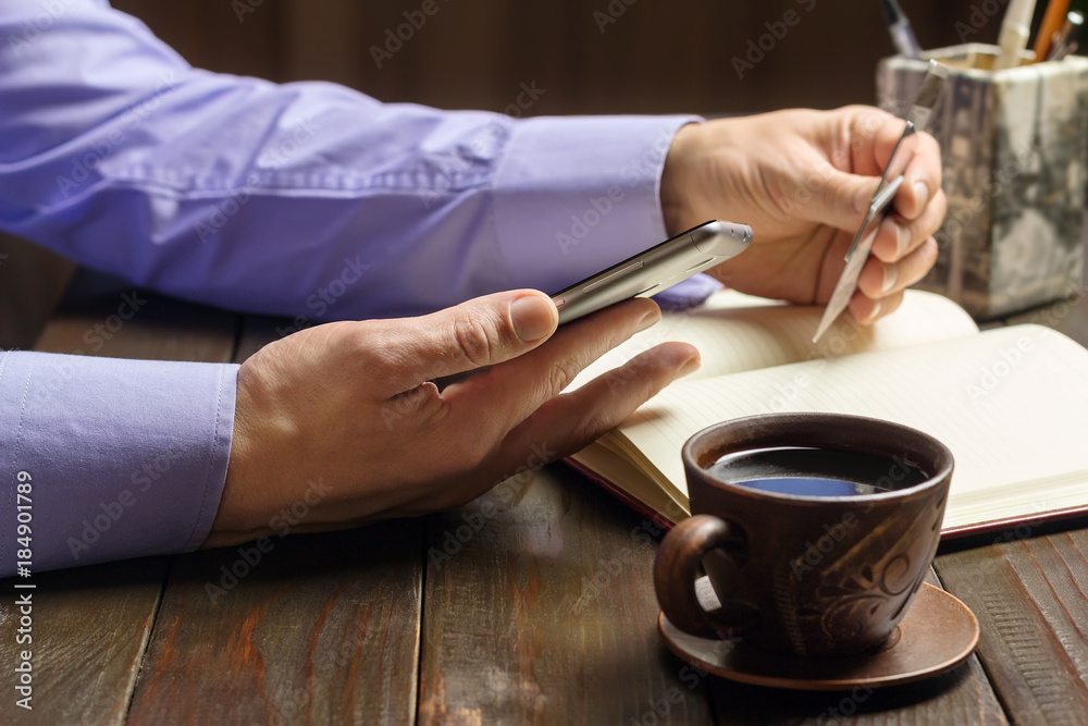 Home office workplace, male hands hold a smartphone and credit card, opened notepad, cup of black coffee on dark wood working table, business, finance concept Home office workplace, male hands hold a smartphone and credit card, opened notepad, cup of black coffee on dark wood working table, business, finance concept