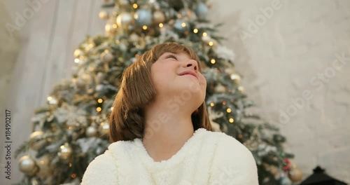 Happy little girl being excited with sparkling colorful confetti falling all around, christmas tree background. Christmas holiday and New Year. photo