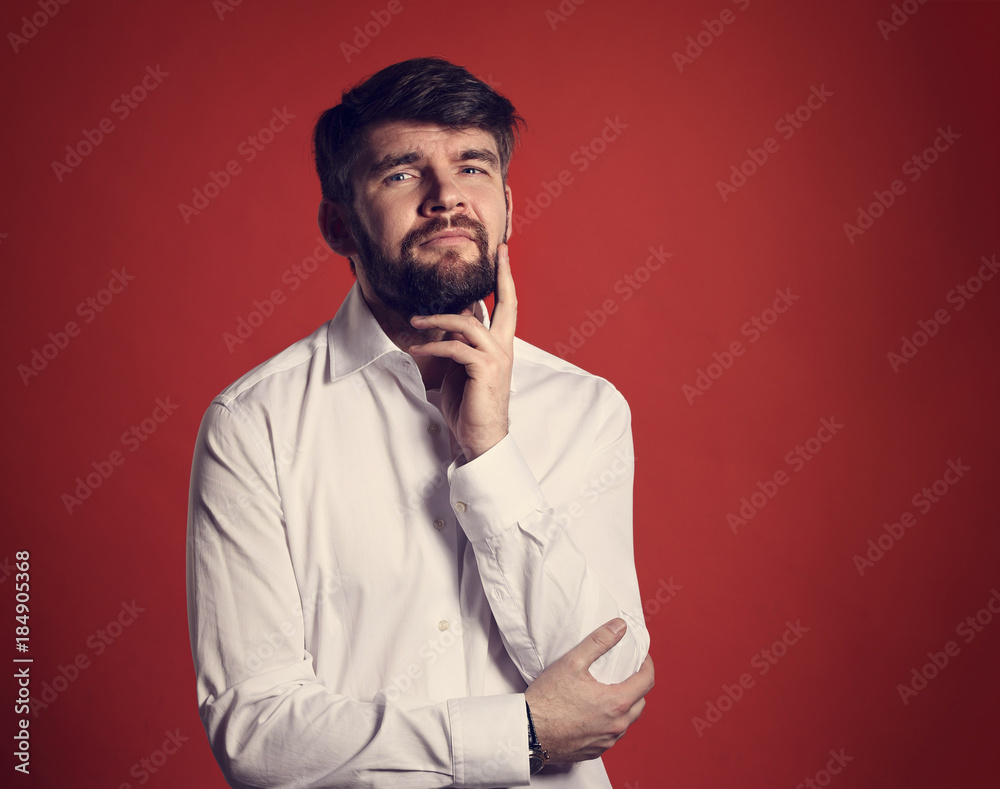 Thinking bearded charismatic man in whirt shirt looking on red background with empty copy space. Closeup portrait Thinking bearded charismatic man in whirt shirt looking on red background with empty copy space. Closeup portrait