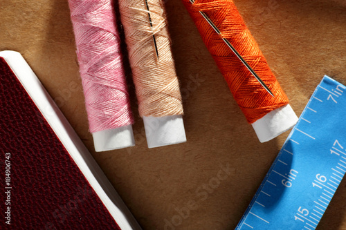 Bright Set Needle, spools with threads, book and blue tape measure with inches and centimeters on paper. Red, blue, white, orange colors.