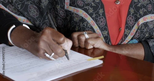 Black senior woman signing her name on legal paperwork with her signature photo