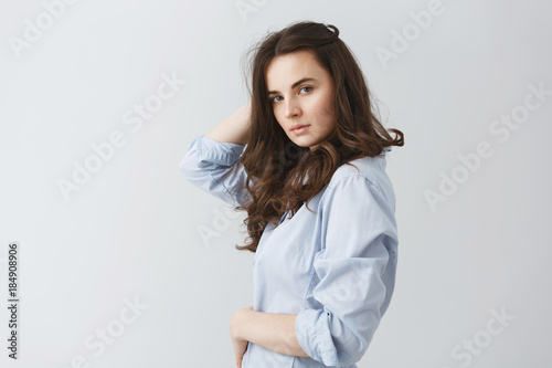 Portrait of fashionable young student girl with dark wavy hair looking in camera with relaxed and confident look, posing for fashion photoshoot.