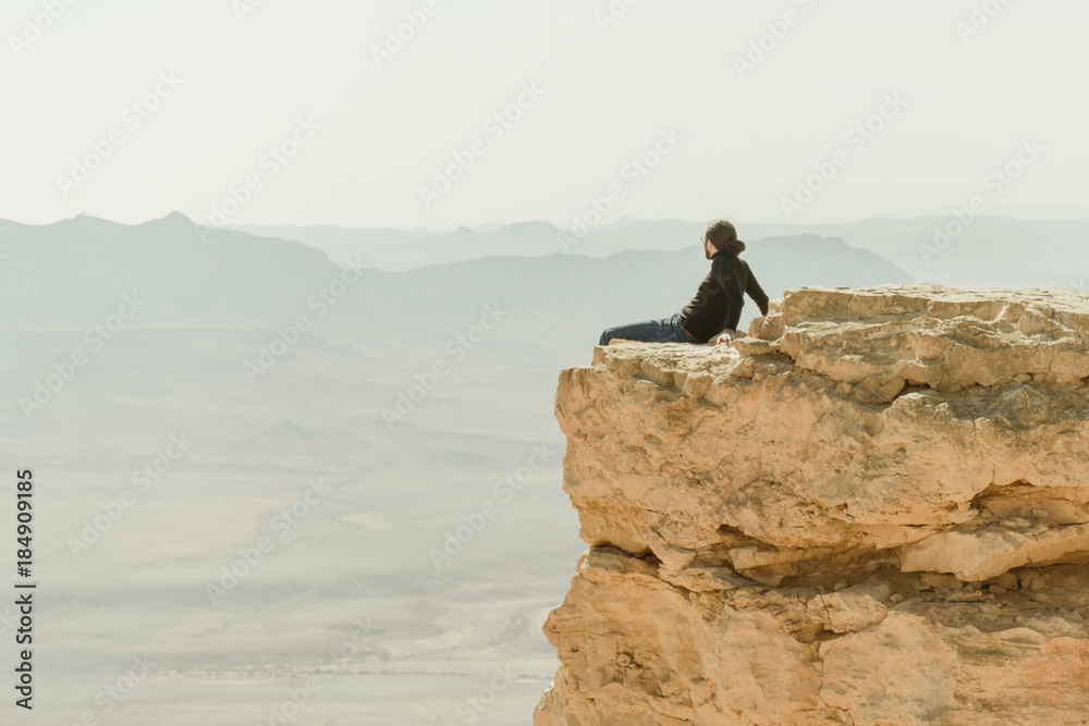 Alone tourist sitting on the edge of cliff and view on desert