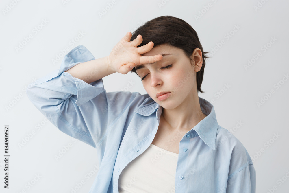 Portrait of good-looking young girl with short hair holding hand on forehead with closed eyes with exhausted expression, tired of head ache. Portrait of good-looking young girl with short hair holding hand on forehead with closed eyes with exhausted expression, tired of head ache.