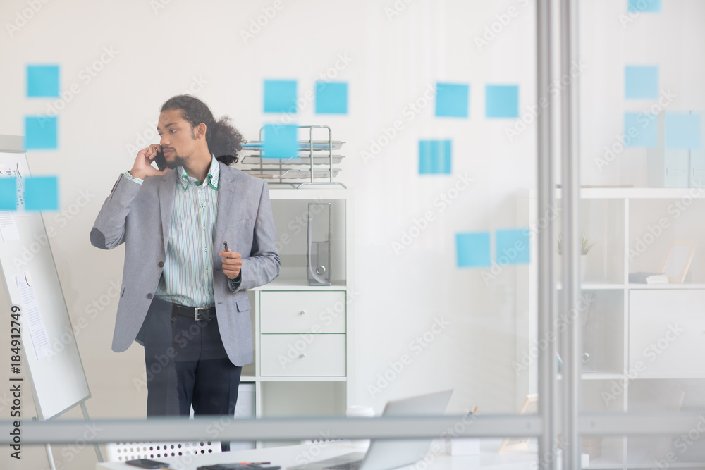 Busy office worker speaking on smartphone and looking at data on whiteboard Busy office worker speaking on smartphone and looking at data on whiteboard