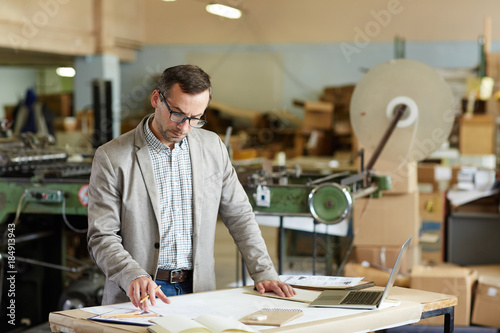 Mature engineer in smart casual looking at one of technical sketches at work