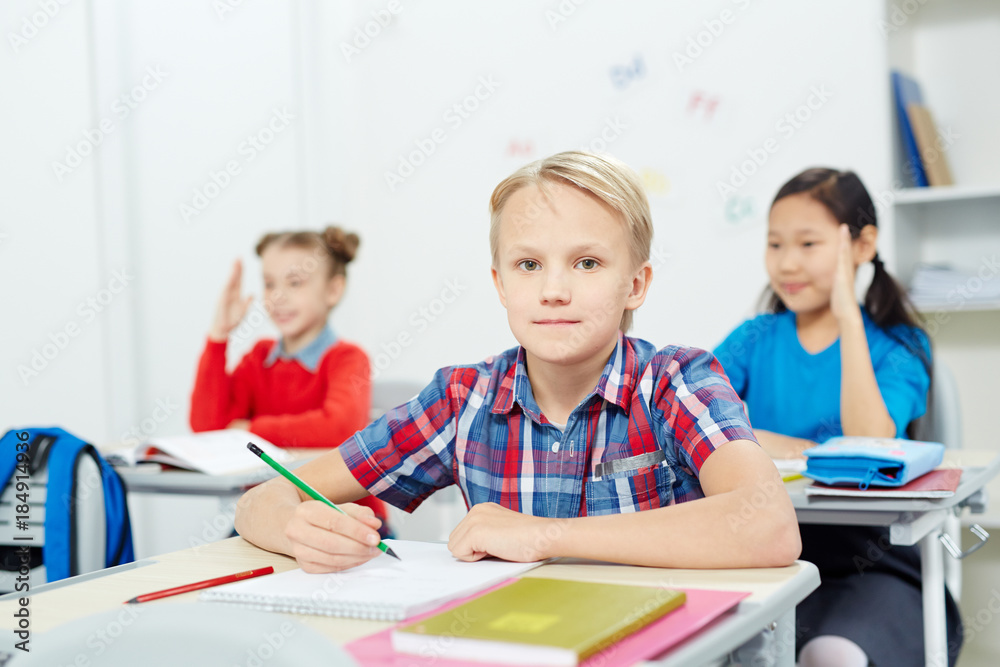 Serious schoolboy with pencil looking at camera by desk while drawing at lesson Serious schoolboy with pencil looking at camera by desk while drawing at lesson