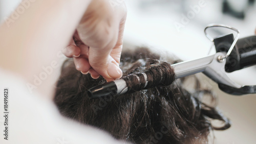A woman in a hairdressing salon. Master twisting curls on short haircut. Only hands.