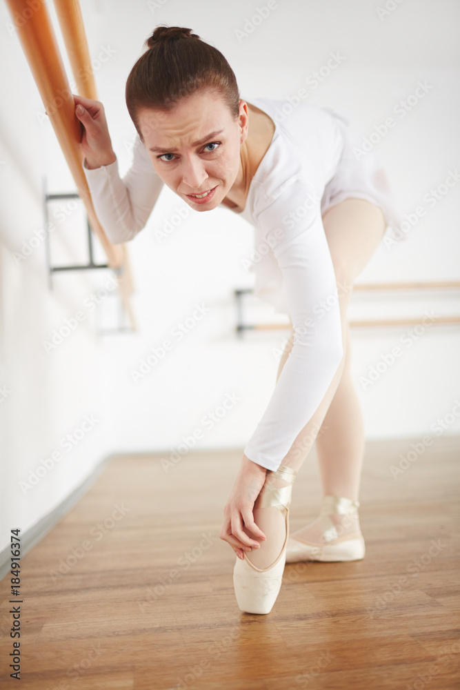 Young ballerina with hand on her hurt foot looking at camera during training