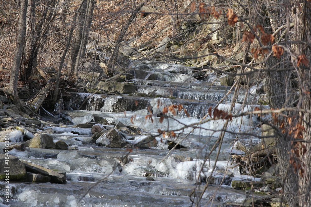 Cascading water down a slight hilly and rocky incline. Ice beginning to form on rocks at the beginning of the winter season.  