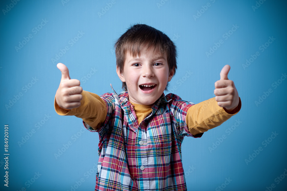 Cheerful Caucasian boy is holding thumbs up and smiling in the camera.