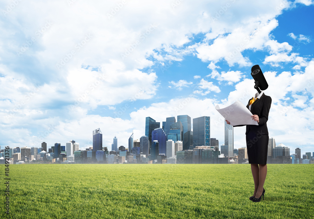 Camera headed woman standing on green grass against modern cityscape