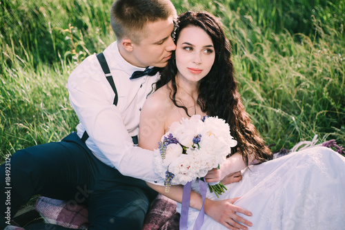 Newlyweds in love are sitting on the grass in the park. the bride and groom smile and have fun at the wedding picnic. Closeup shot.