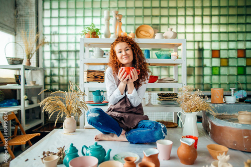 Beautiful redhead woman sitting in lotus pose in clay shop photo