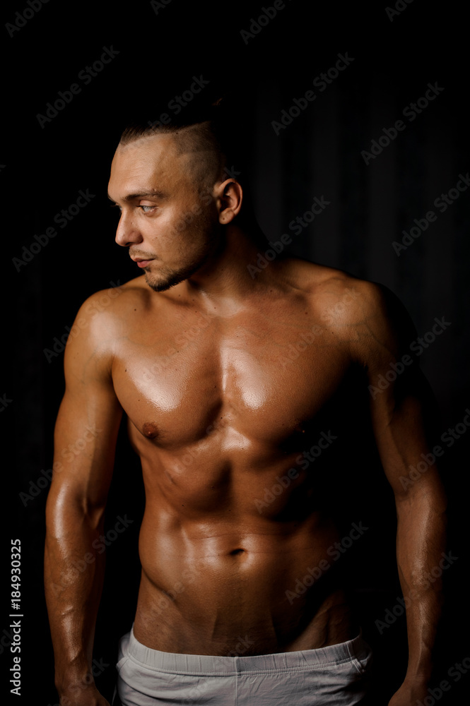 Shirtless muscular and tanned bodybuilder guy on the black background Shirtless muscular and tanned bodybuilder guy on the black background
