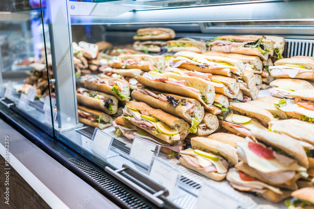 Display of many large sandwiches behind glass window of store stuffed with ham, cheese and cucumbers