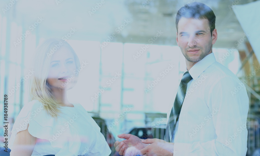 Obraz premium Two cheerful smiling young businesspeople talking at the office. View through window