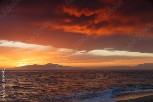 Crimson sunset on the shore of the orange sky and calm sea witt view at the mountains