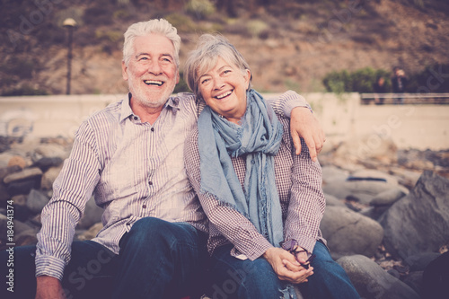 gentlemen couple sitting at the beach at sunset. smile and happy lifestyle for aged mature caucasian people in outdoor leisure activity. hug and love forever