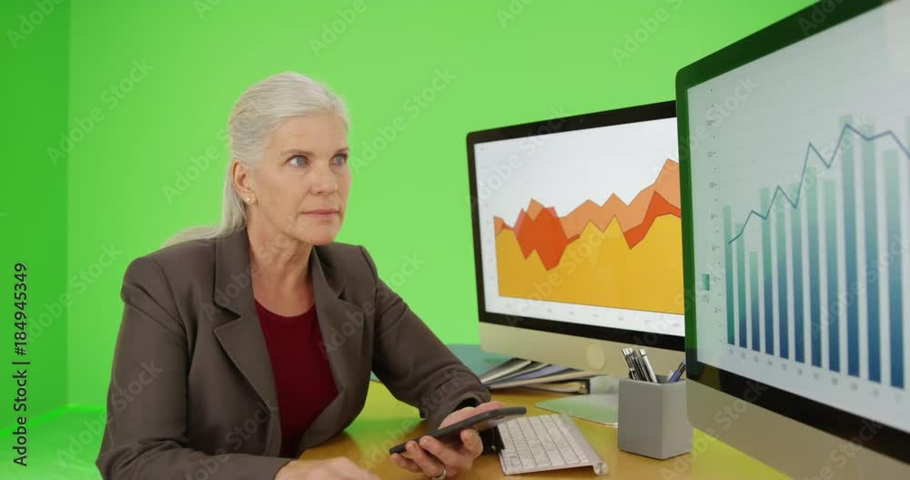 An older businesswoman uses her smart phone on green screen. On green screen to be keyed or composited. An older businesswoman uses her smart phone on green screen. On green screen to be keyed or composited.