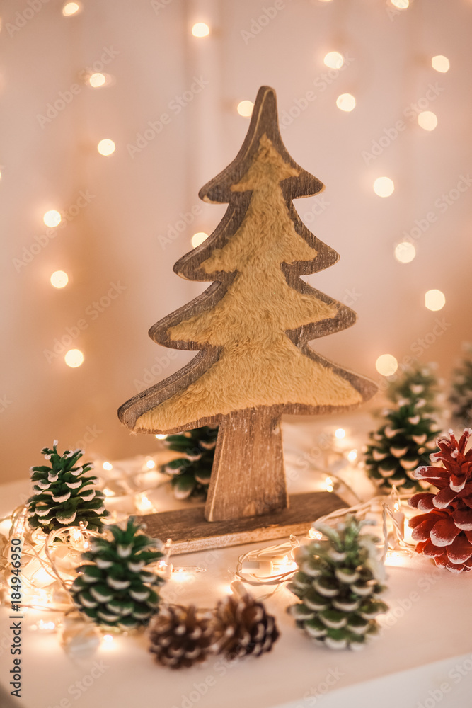 Closeup of cute elements of cozy winter Xmas interior. Wooden decorative tree decorated with faux fur, painted pine cones and electrical garlands on windowsill. Vertical color photography.