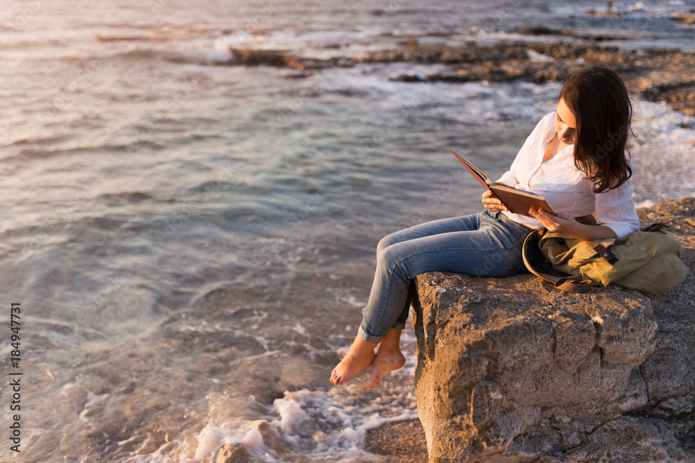 teenage girl reading book on the beach in sunset
