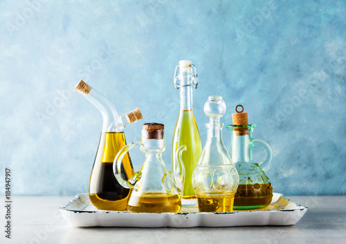 different shapes, types and sizes of cruets with olive oil on the table on a tray on blue